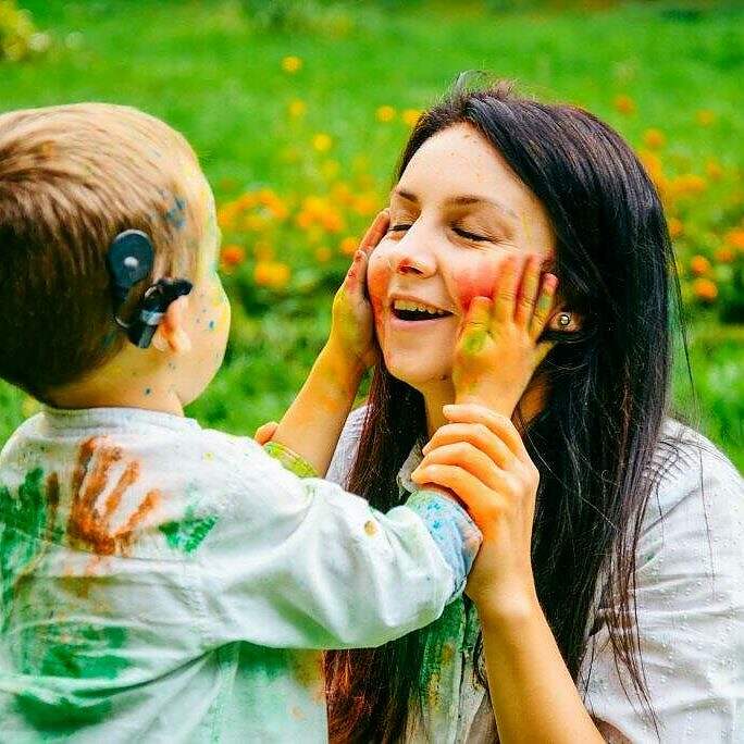 Happy mother and son playing with holi paints in city park